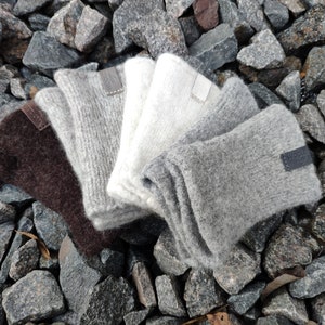 May include: Four pairs of fingerless gloves in different shades of gray, brown, and white. The gloves are made of a soft, fuzzy material and have leather labels with the word "Wool" on them.