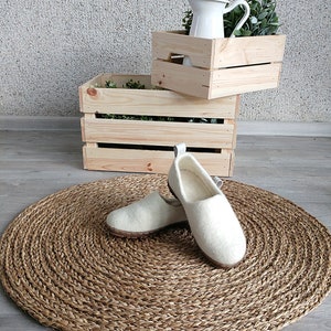 Peut inclure: Deux paires de pantoufles en laine blanche sur un tapis rond tiss&eacute;. Les pantoufles ont un design simple et sont faites d'un mat&eacute;riau doux et confortable.