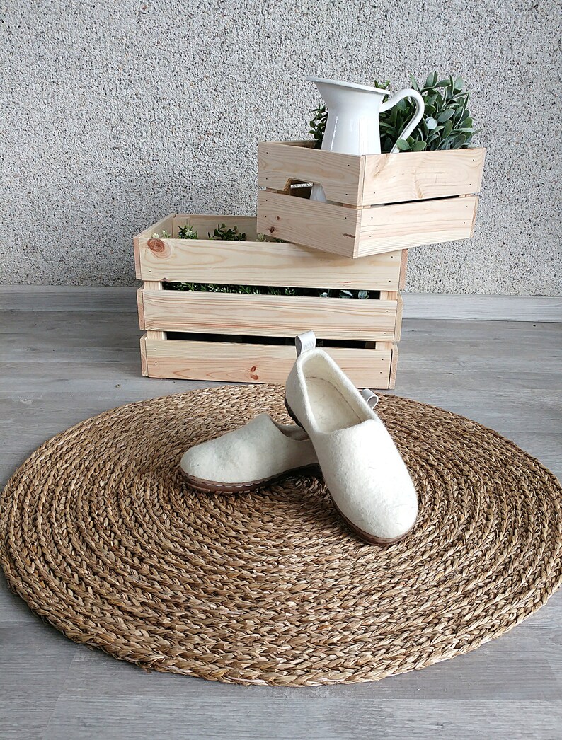 Peut inclure: Deux paires de pantoufles en laine blanche sur un tapis rond tiss&eacute;. Les pantoufles ont un design simple et sont faites d'un mat&eacute;riau doux et confortable.