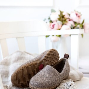 Peut inclure: Une paire de pantoufles en feutre marron avec des semelles en caoutchouc, pos&eacute;es sur une chaise blanche avec un jet&eacute; en lin. Les pantoufles sont sur une chaise blanche avec un jet&eacute; en lin.