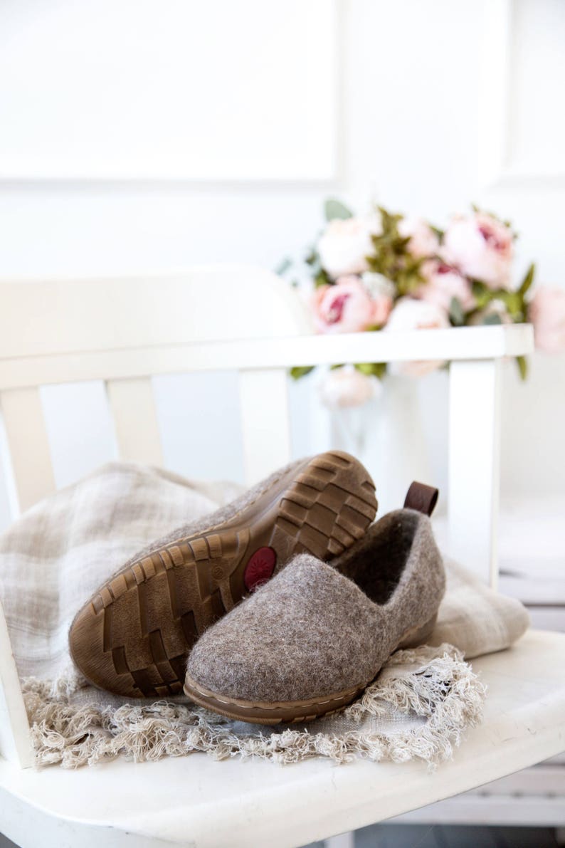 Peut inclure: Une paire de pantoufles en feutre marron avec des semelles en caoutchouc, pos&eacute;es sur une chaise blanche avec un jet&eacute; en lin. Les pantoufles sont sur une chaise blanche avec un jet&eacute; en lin.