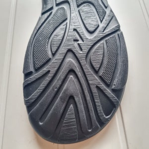May include: Close-up of the black rubber sole of a shoe with a textured pattern.