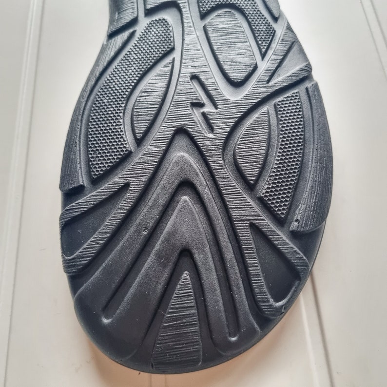 May include: Close-up of the black rubber sole of a shoe with a textured pattern.