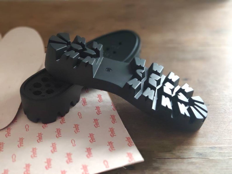 Puede incluir: Dos suelas de zapatos de goma negra con un patr&oacute;n de banda de rodadura texturizado. Las suelas est&aacute;n dise&ntilde;adas para uso en exteriores y tienen un aspecto robusto.