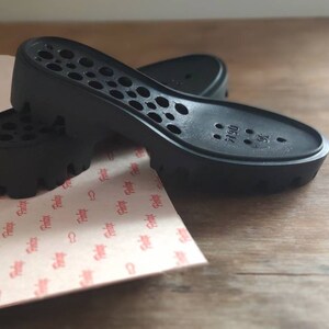 Puede incluir: Dos plantillas de zapatos negras con un patr&oacute;n de panal y el texto "0514 38" en la parte inferior.