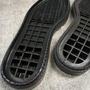 May include: Close-up of the black rubber soles of two shoes. The soles have a grid pattern and a textured edge.