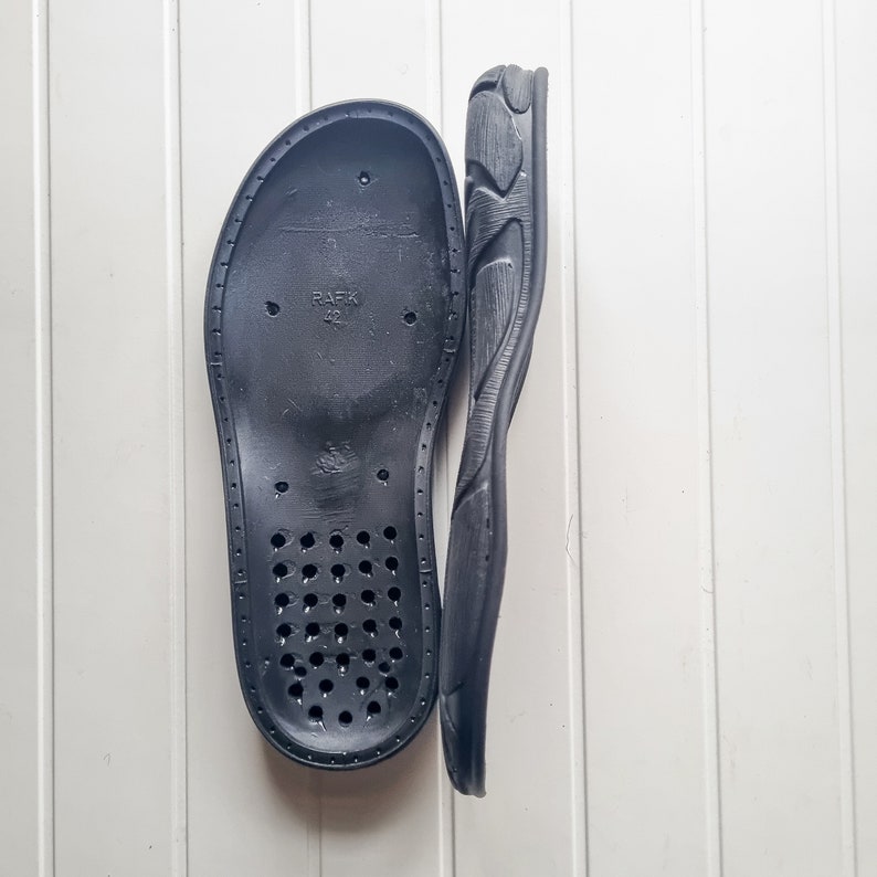 May include: A black shoe insole with a textured surface and a series of small holes. The insole has the text "PAFK 42" printed on it.