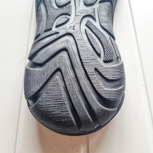 May include: Close-up of the black rubber sole of a shoe with a textured pattern and the number "42" printed on it.