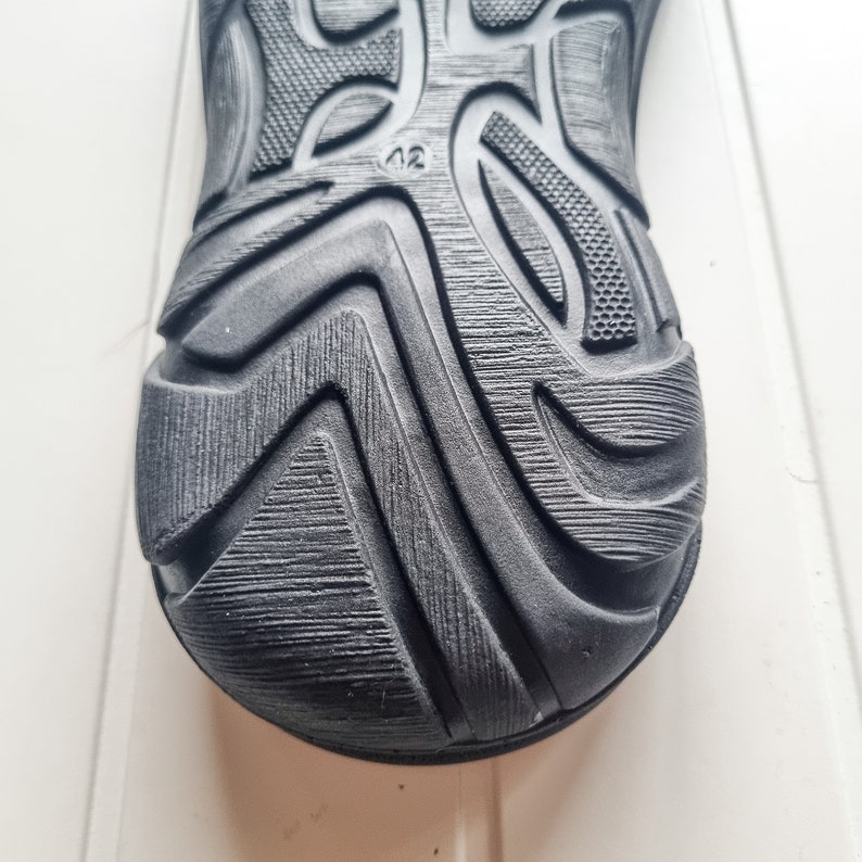 May include: Close-up of the black rubber sole of a shoe with a textured pattern and the number "42" printed on it.