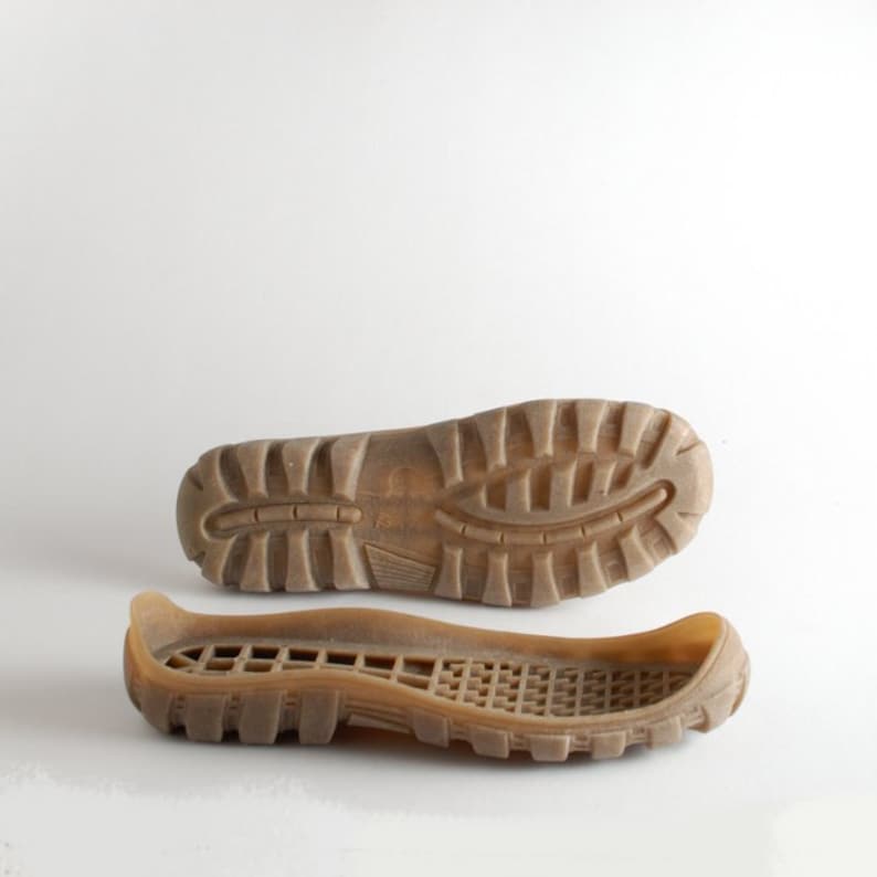 May include: A pair of brown rubber shoe soles. The top sole has a textured tread pattern. The bottom sole is a flexible, moulded rubber with a grid pattern.