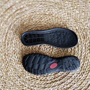 Puede incluir: Dos suelas de zapatos negras, una con un patr&oacute;n texturizado y la otra con una superficie lisa. Las suelas est&aacute;n sobre una estera de paja tejida.
