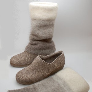 May include: A pair of brown wool slippers with a white and brown wool boot cuff. The slippers have a rounded toe and a low heel. The boot cuff is folded down and has a white, gray, and brown ombre pattern.