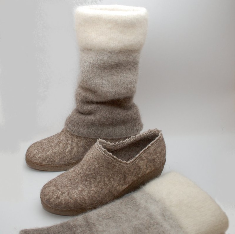 May include: A pair of brown wool slippers with a white and brown wool boot cuff. The slippers have a rounded toe and a low heel. The boot cuff is folded down and has a white, gray, and brown ombre pattern.
