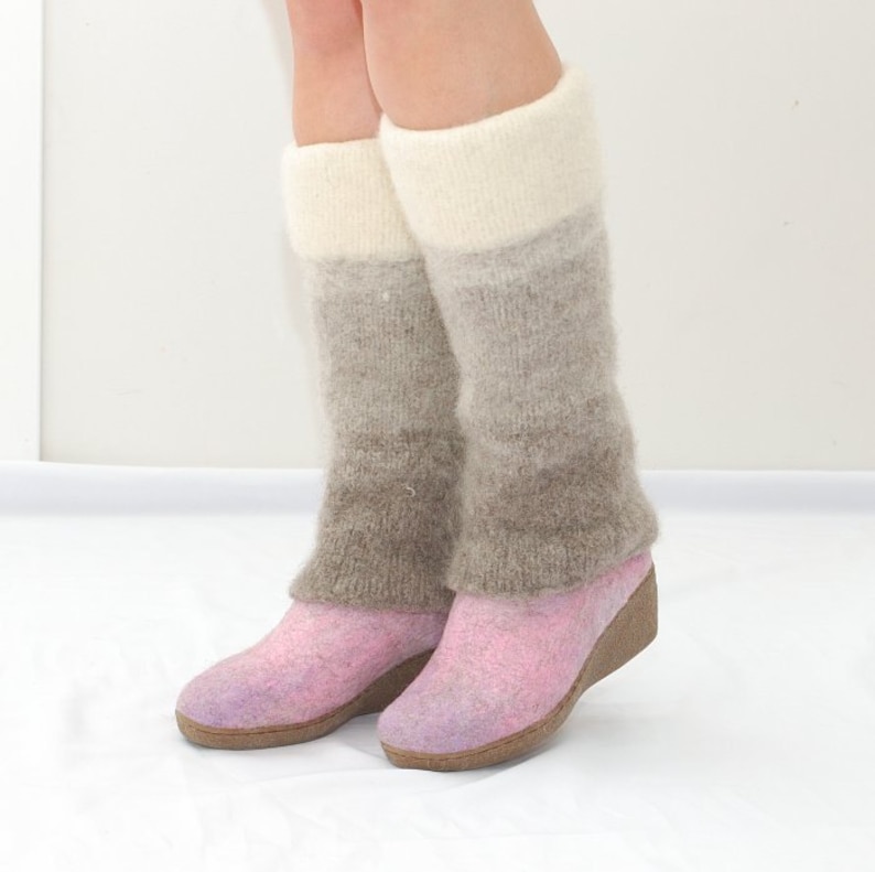May include: A pair of pink felt boots with a wedge heel. The boots are worn with long, brown and white knit leg warmers.