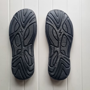 May include: A pair of black rubber soles with a textured pattern. The soles are designed for outdoor use.