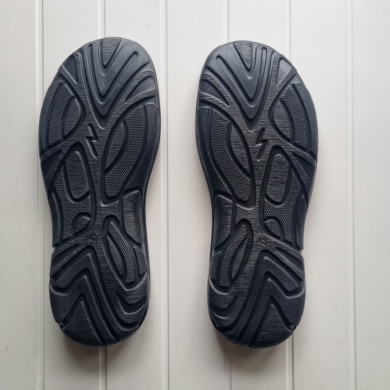 May include: A pair of black rubber soles with a textured pattern. The soles are designed for outdoor use.