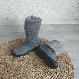 May include: A pair of grey wool boots with black rubber soles. The boots are sitting on a round, woven rug.