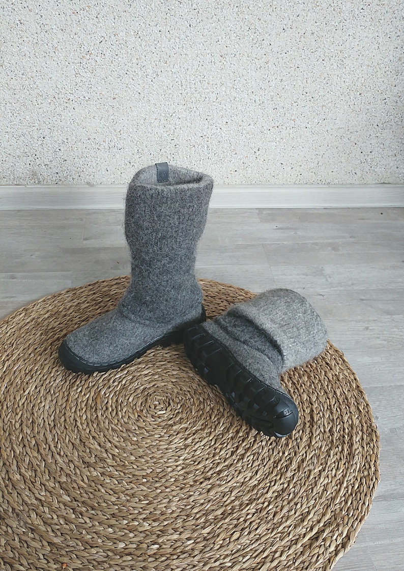 May include: A pair of grey wool boots with black rubber soles. The boots are sitting on a round, woven rug.