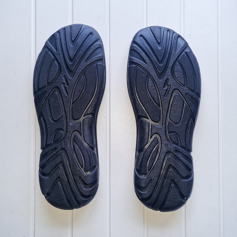 May include: A pair of black rubber soles with a textured pattern. The soles have a raised design with a lightning bolt symbol.