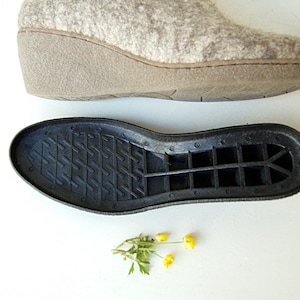 May include: A pair of gray felt slippers with a black rubber sole. The sole has a grid pattern and a raised heel.