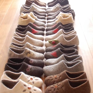 Pode incluir: Uma cole&ccedil;&atilde;o de 20 pares de pantufas de l&atilde; em v&aacute;rios tons de marrom, cinza e branco. As pantufas t&ecirc;m padr&otilde;es e designs diferentes, incluindo florais, geom&eacute;tricos e abstratos.