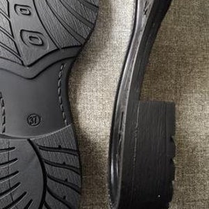Könnte beinhalten: Ein Paar schwarze Schuhsohlen, eine mit einem strukturierten Profil und die andere mit einem dickeren Blockabsatz. Die Sohle links hat die Größe 37 aufgedruckt.