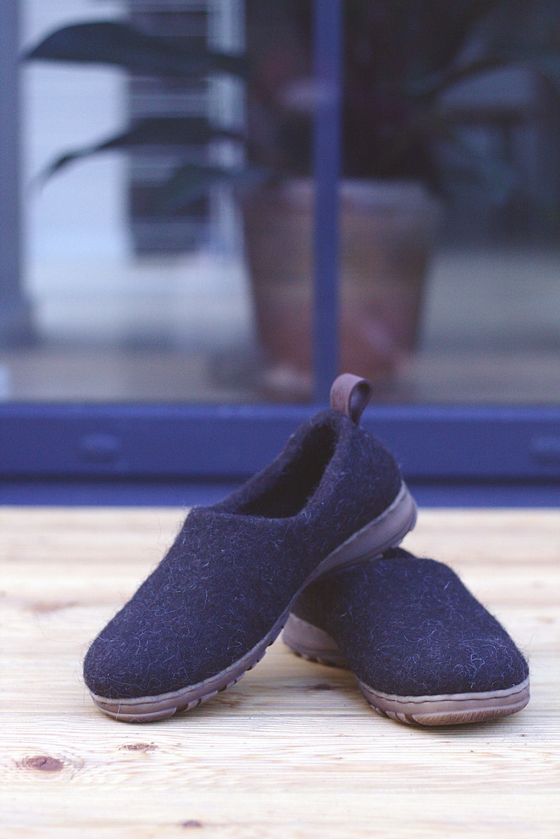 Peut inclure: Une paire de pantoufles en laine noire avec des semelles brunes. Les pantoufles sont sur une surface en bois.
