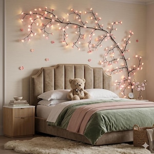 Könnte beinhalten: Ein Schlafzimmer mit einem Bett mit beigem Kopfteil, weißer Bettwäsche und einer grünen Samt-Bettdecke. Ein Teddybär sitzt auf dem Bett. Ein dekorativer floraler Zweig mit rosa Lichtern ziert die Wand. Ein kleiner Nachttisch und ein Teppich.