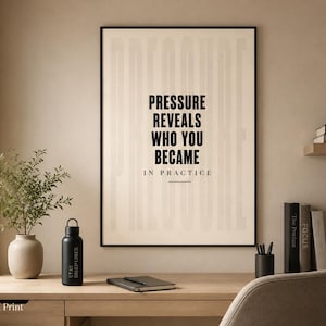 May include: A framed print with the text "PRESSURE REVEALS WHO YOU BECAME IN PRACTICE" hangs above a wooden desk. A black water bottle with "STAY DISCIPLINED" is on the desk, along with a notebook, pen holder, and books.