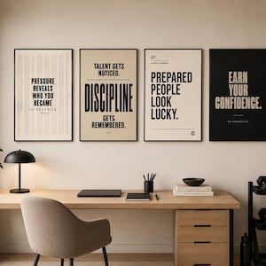 May include: Four framed motivational posters with black frames hang above a desk. The posters have white and black backgrounds with text that reads: "Pressure Reveals Who You Became", "Talent Gets Noticed. Discipline Gets Remembered.", "Prepared People Look Lucky.", and "Earn Your Confidence."