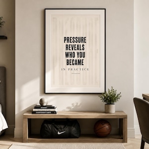 May include: A framed print with the text "PRESSURE REVEALS WHO YOU BECAME IN PRACTICE" hangs above a wooden bench. A black Nike duffel bag and a basketball sit on the bench. A basketball and a plant are on a shelf.