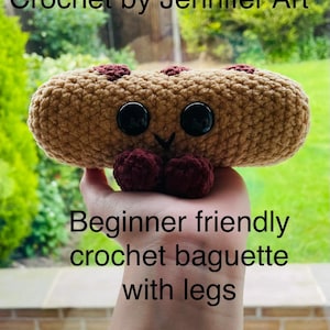May include: A handmade crocheted baguette with black button eyes and burgundy accents. The bread-shaped item has two burgundy pom-pom legs. Text on the image reads "Crochet by Jennifer Art" and "Beginner friendly crochet baguette with legs."