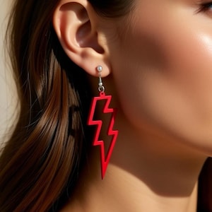 May include: Red lightning bolt earrings. These earrings have a striking, cutout design in a bright red hue. The earrings are suspended from a silver-coloured hook.