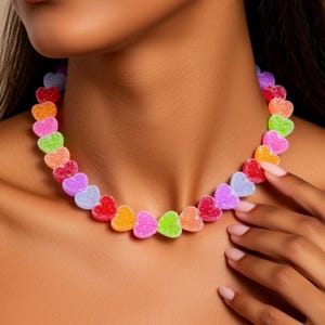 May include: A colorful necklace made of heart-shaped candies in various colors, including red, orange, pink, green, and purple. The necklace is worn around the neck, creating a playful and vibrant accessory.