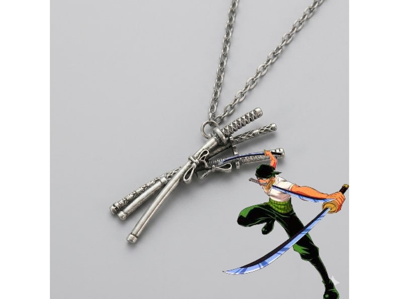 May include: Silver-toned necklace featuring a pendant of three crossed swords. The swords have detailed handles and blades. A cartoon illustration of a character wielding swords is in the lower right corner.