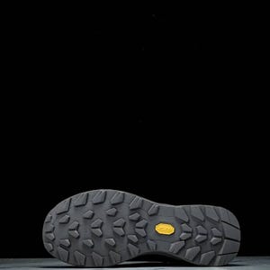 May include: Close-up of the sole of a dark grey hiking shoe. The sole has a textured pattern with a yellow Vibram logo. The shoe is designed for outdoor activities, providing grip and support.