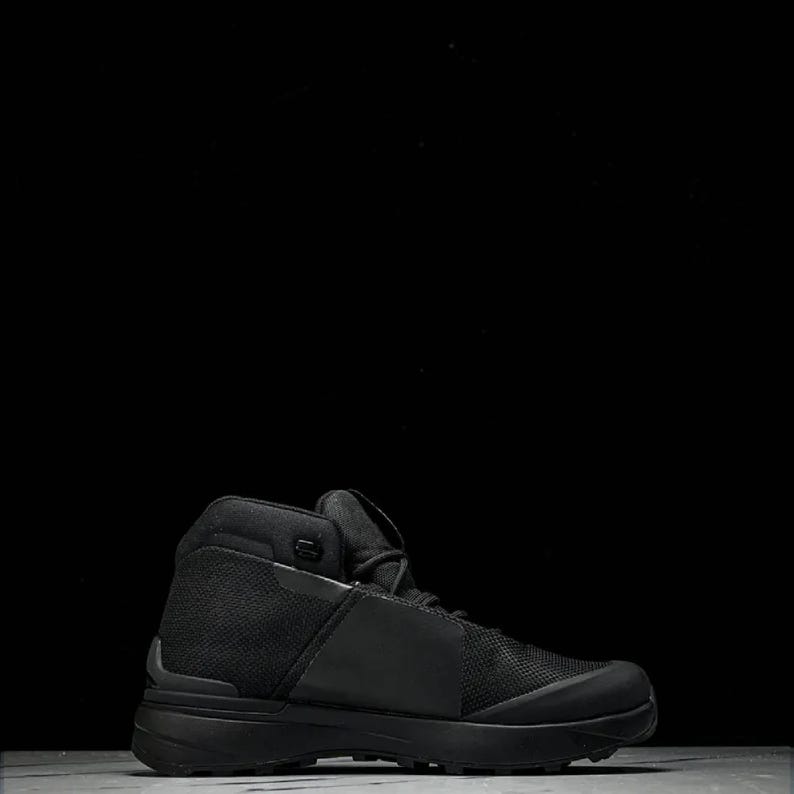 May include: Black high-top hiking boot with a mesh and leather design. The boot features a thick sole and a padded collar for ankle support. The overall design is sleek and modern, suitable for outdoor activities.