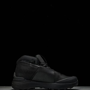 May include: Black high-top hiking boot. The boot has a mesh and smooth material construction, a thick sole, and a padded collar. Designed for outdoor use, it offers ankle support. The boot's design is modern and functional.