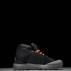 May include: Black and grey hiking boot with orange laces. The boot features a mesh upper and a grey sole. The design is modern and sleek, suitable for outdoor activities. The boot is shown against a black background.