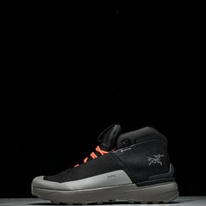 May include: Black and grey hiking boot with orange laces. The boot features a mesh upper, a grey sole, and the word "KOPEC" is printed on the side. The Arc'teryx logo is visible. Designed for outdoor activities, it has a Gore-Tex label.