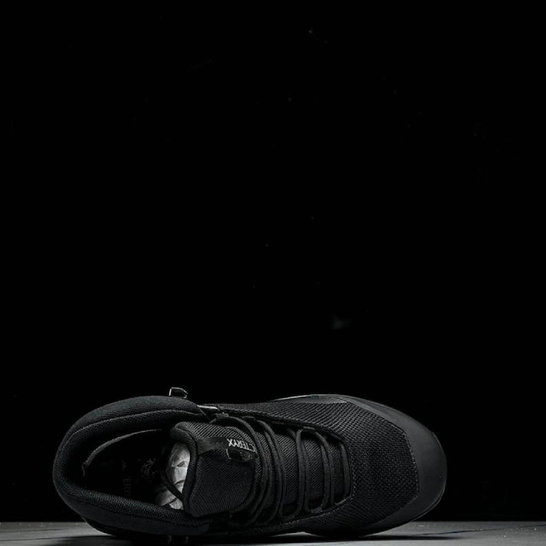 May include: Black athletic shoe with a mesh upper and a thick sole. The shoe features a lace-up design and a padded collar. The shoe is designed for outdoor activities and is suitable for various terrains.