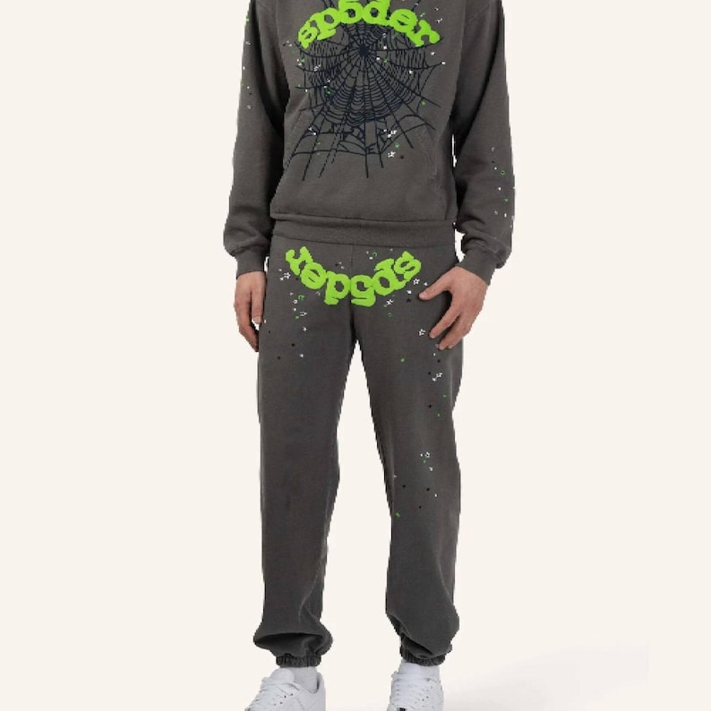 May include: A gray sweatsuit with the word "spider" in green, and a spiderweb graphic on the sweatshirt. The sweatpants and sweatshirt have a speckled design. The person is wearing white sneakers.