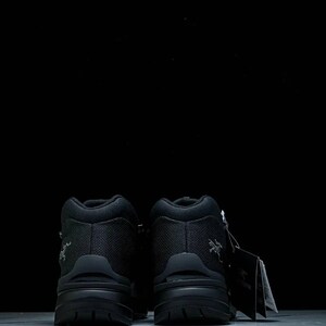 May include: Two black hiking boots with a textured upper and a chunky sole. The boots are high-top and feature a small logo. A tag is attached to the right boot.