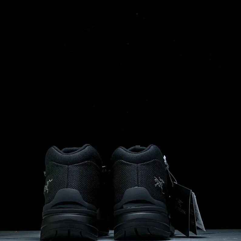 May include: Two black hiking boots with a textured upper and a chunky sole. The boots are high-top and feature a small logo. A tag is attached to the right boot.