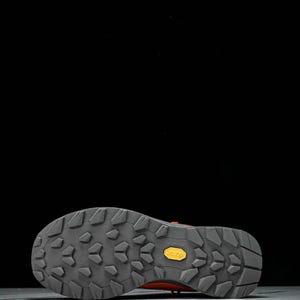 May include: Close-up of the sole of a hiking boot. The sole is grey with a textured pattern and a yellow "Vibram" logo. The boot's upper is a reddish-orange colour.