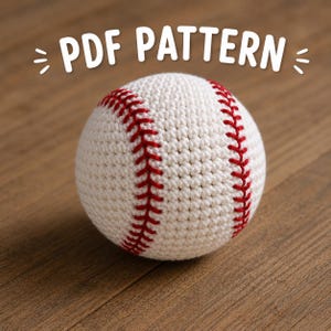 Puede incluir: Una pelota de béisbol de ganchillo con costuras rojas sobre una superficie de madera. El texto "PDF PATTERN" se muestra encima de la pelota. La pelota es blanca con costuras rojas.