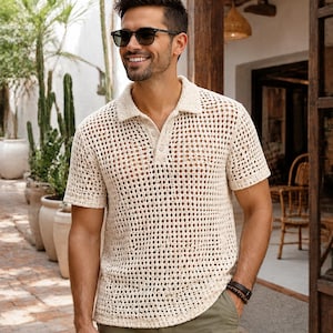Può includere: Una polo a maniche corte color crema caratterizzata da una trama all'uncinetto a maglia aperta, con colletto classico e abbottonatura a tre bottoni. Il capo è abbinato a pantaloncini verde oliva, creando un completo dai toni neutri.