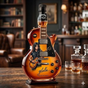 May include: A glass bottle shaped like an electric guitar with an amber liquid inside. The bottle features a graphic of a person playing a guitar, the text J.H. DISTILLERY No.2, the word glala, and the phrase Rock N' Roll Legend with black knobs.