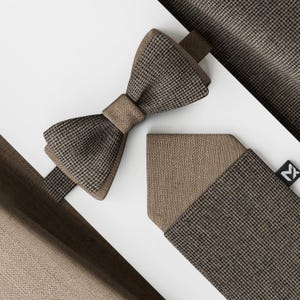 May include: A brown and black houndstooth bow tie, pocket square, and fabric swatch. The bow tie is centered, with the pocket square and fabric swatch arranged around it. The items are set against a white background.