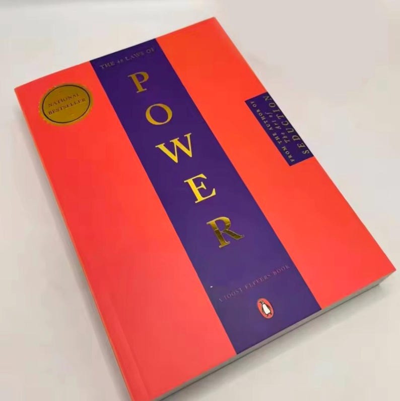 May include: A hardback book titled "The 48 Laws of Power" with a red cover and a purple vertical stripe. The word "POWER" is in gold lettering. A gold sticker reads "National Bestseller".